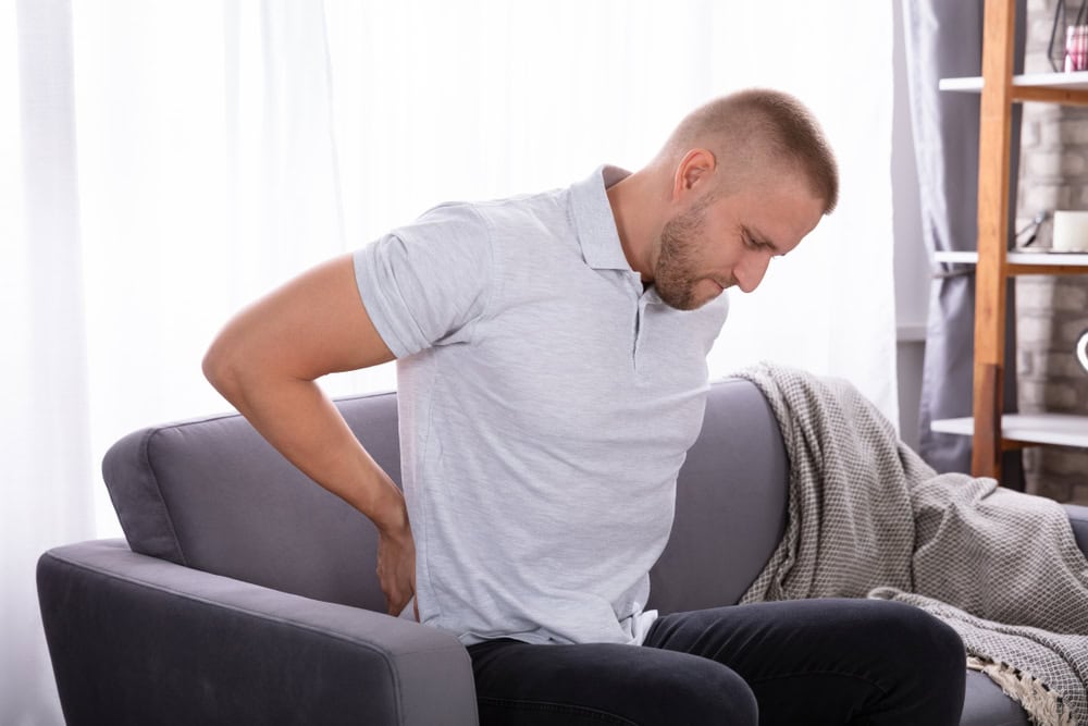 Young,Man,Sitting,On,Sofa,Suffering,From,Back,Pain